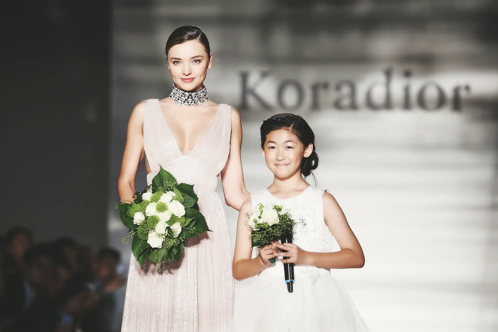 Miranda Kerr walking the runway beside a young flower girl