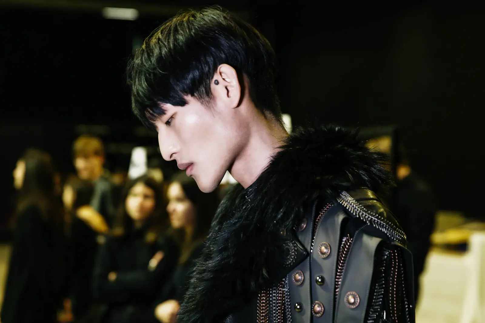 Male model in fur and studded leather, seen in profile backstage