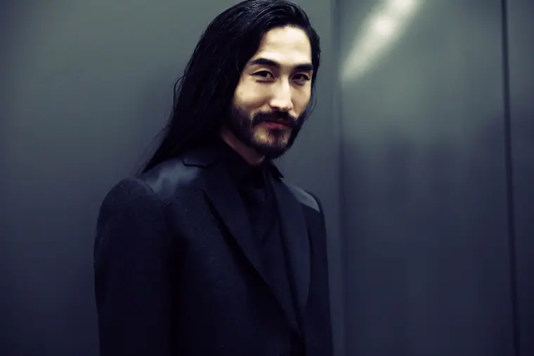 Male model with long dark hair and a beard in a dark suit
