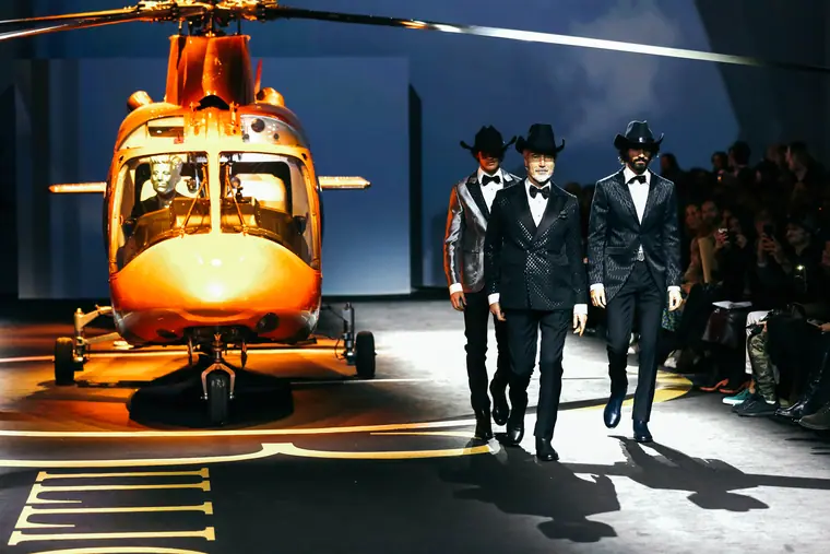 Models in suits walking past a helicopter on stage