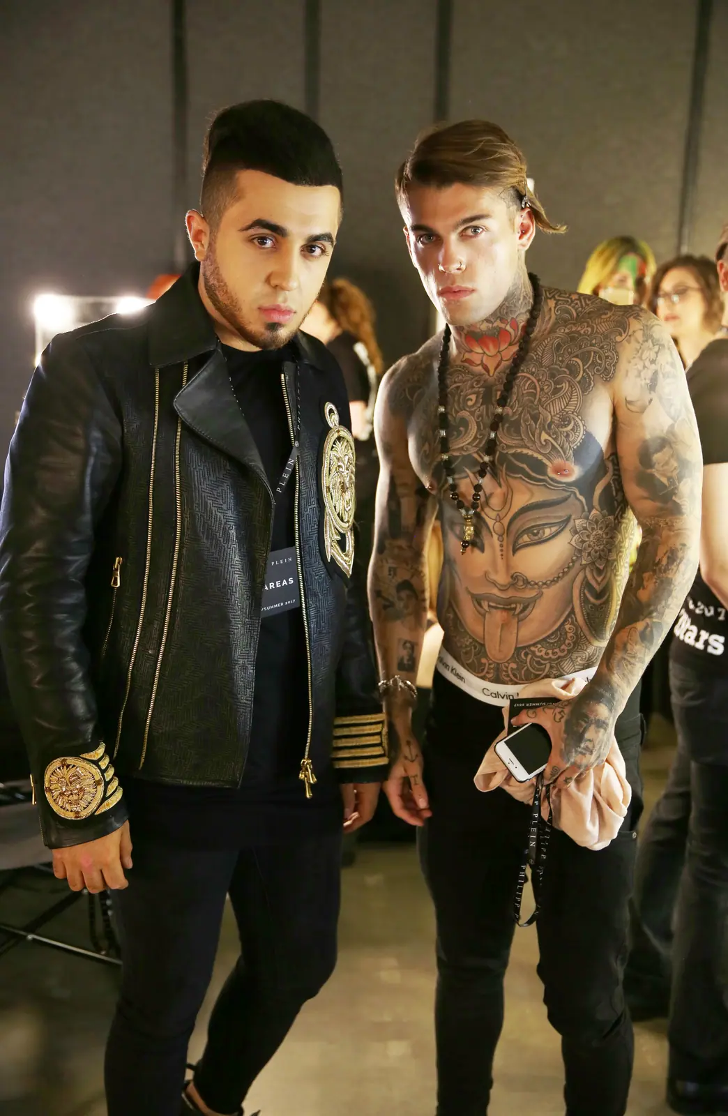 Two male models backstage, one heavily tattooed