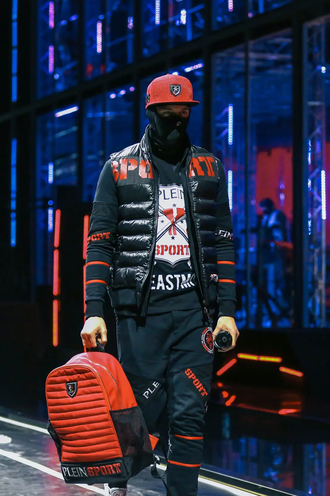 Model in a red cap and puffer jacket on a neon-lit runway
