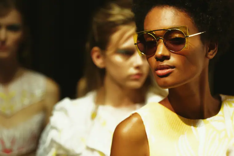 Models backstage, one in sunglasses, in warm light