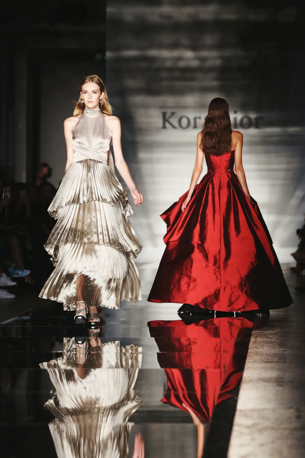 Two models in red and ivory gowns on a reflective runway