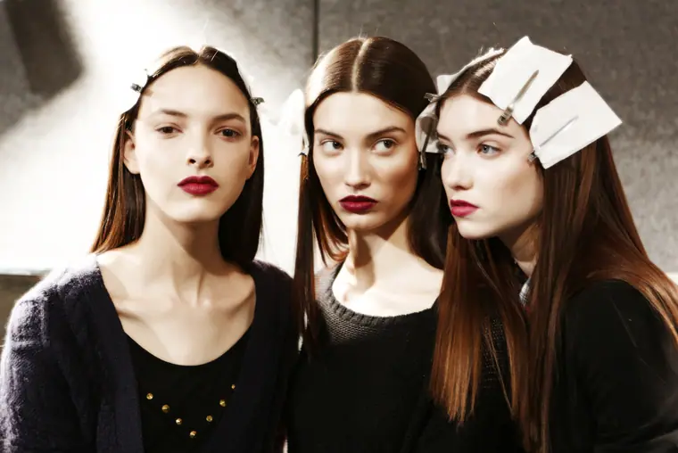 Three models with dark hair and red lips, backstage