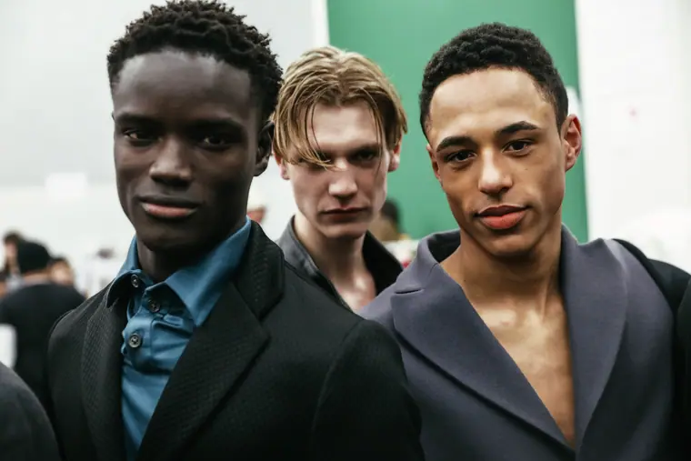 Three male models in dark tailoring, backstage