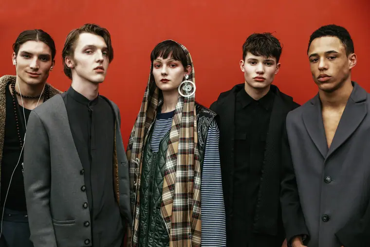 Male models in grey tailoring against a red wall