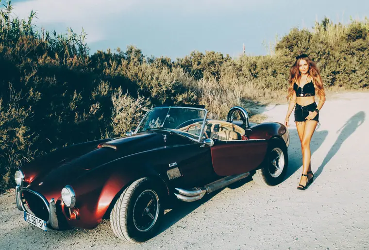 Elisha beside a vintage roadster on a dirt road