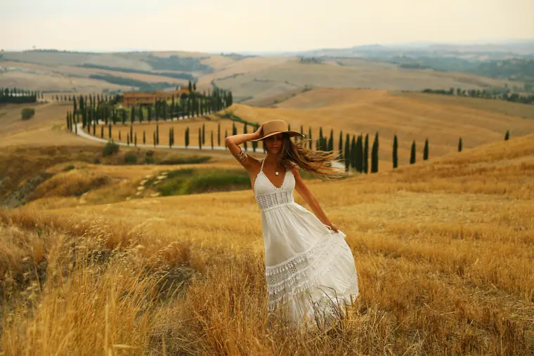 Elisha in a white dress and straw hat in a Tuscan wheat field, cypress-lined road behind her