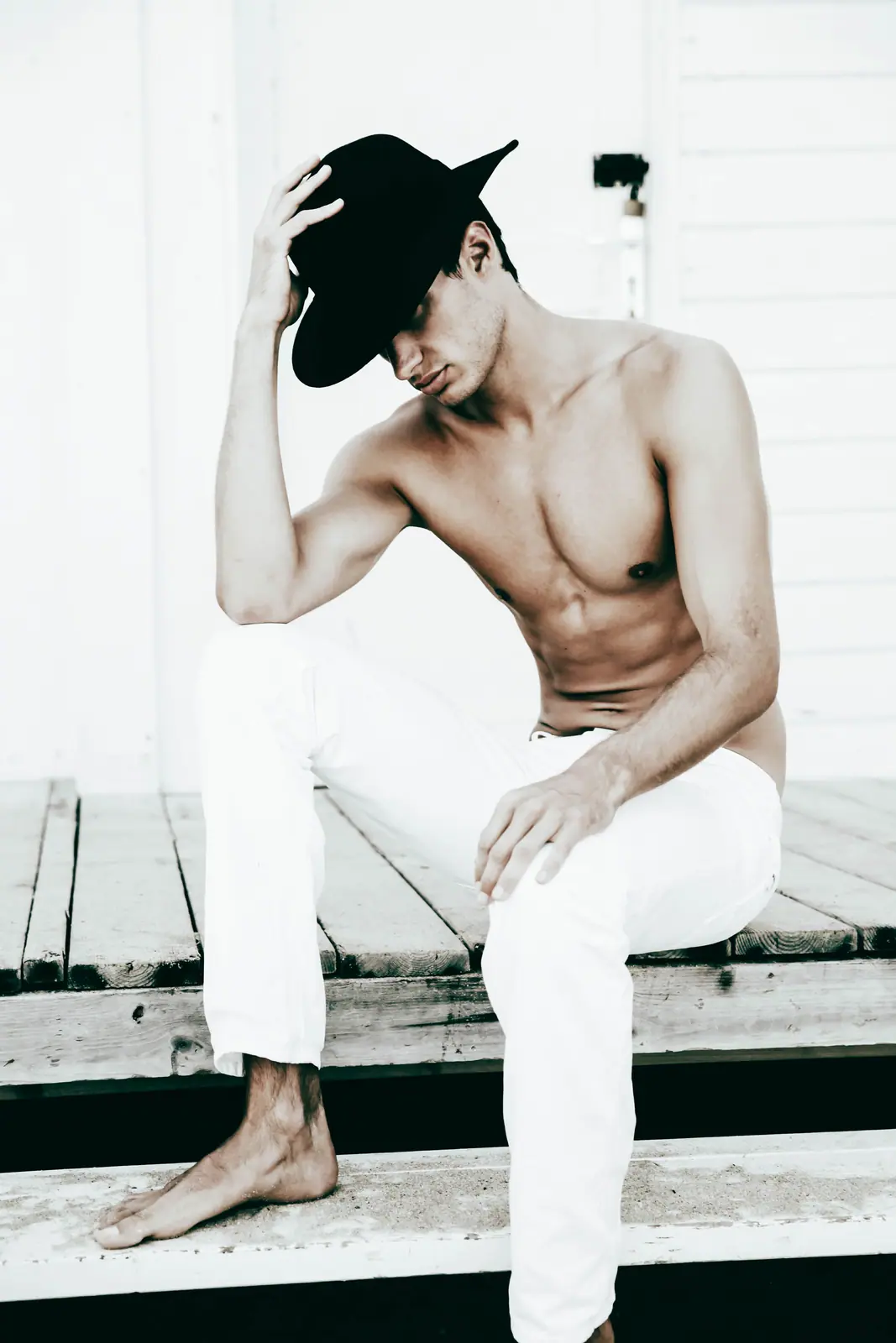 Shirtless man in a black hat seated on white steps
