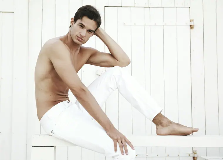 Shirtless man in white trousers by a white door