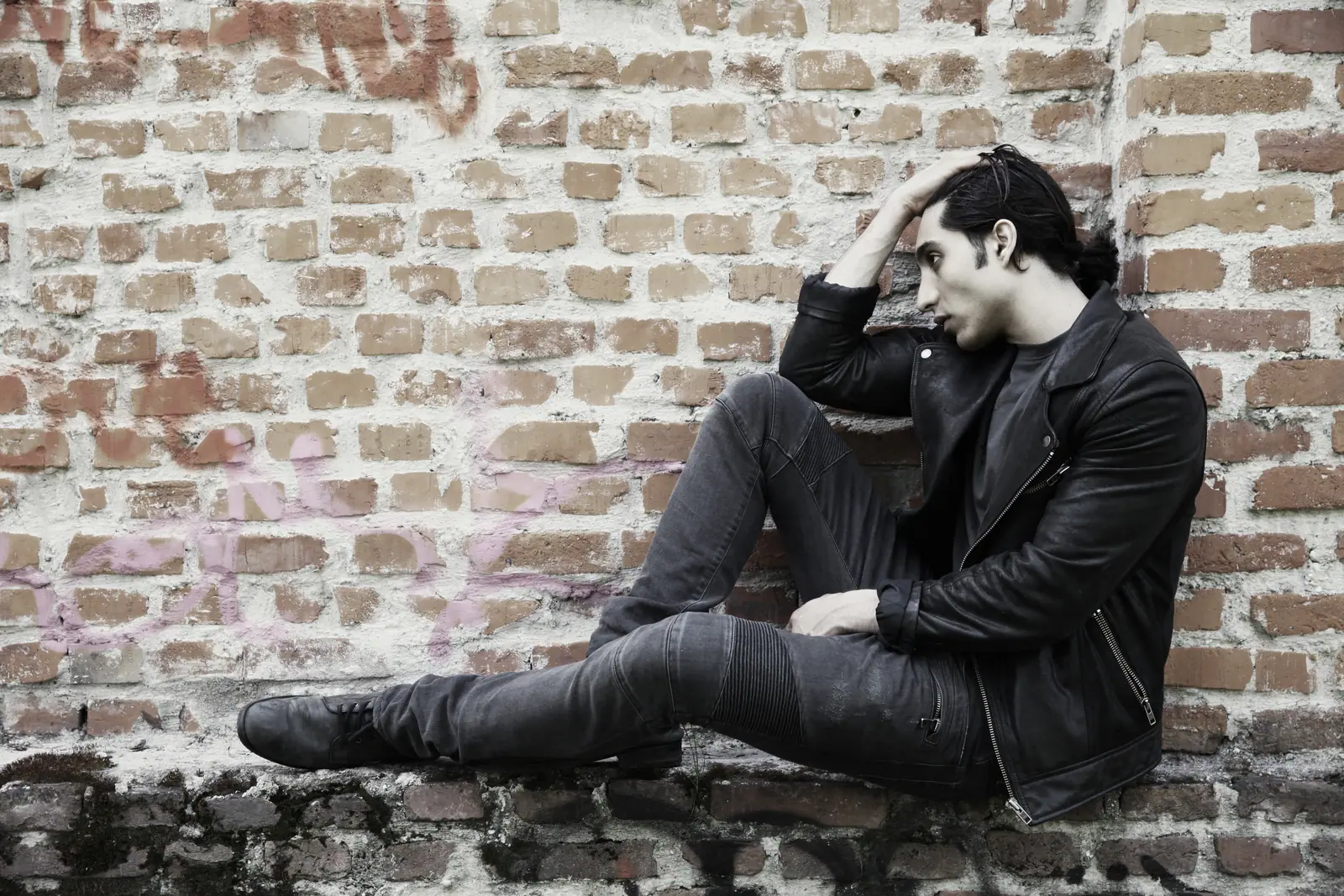 Man in a leather jacket against a brick wall